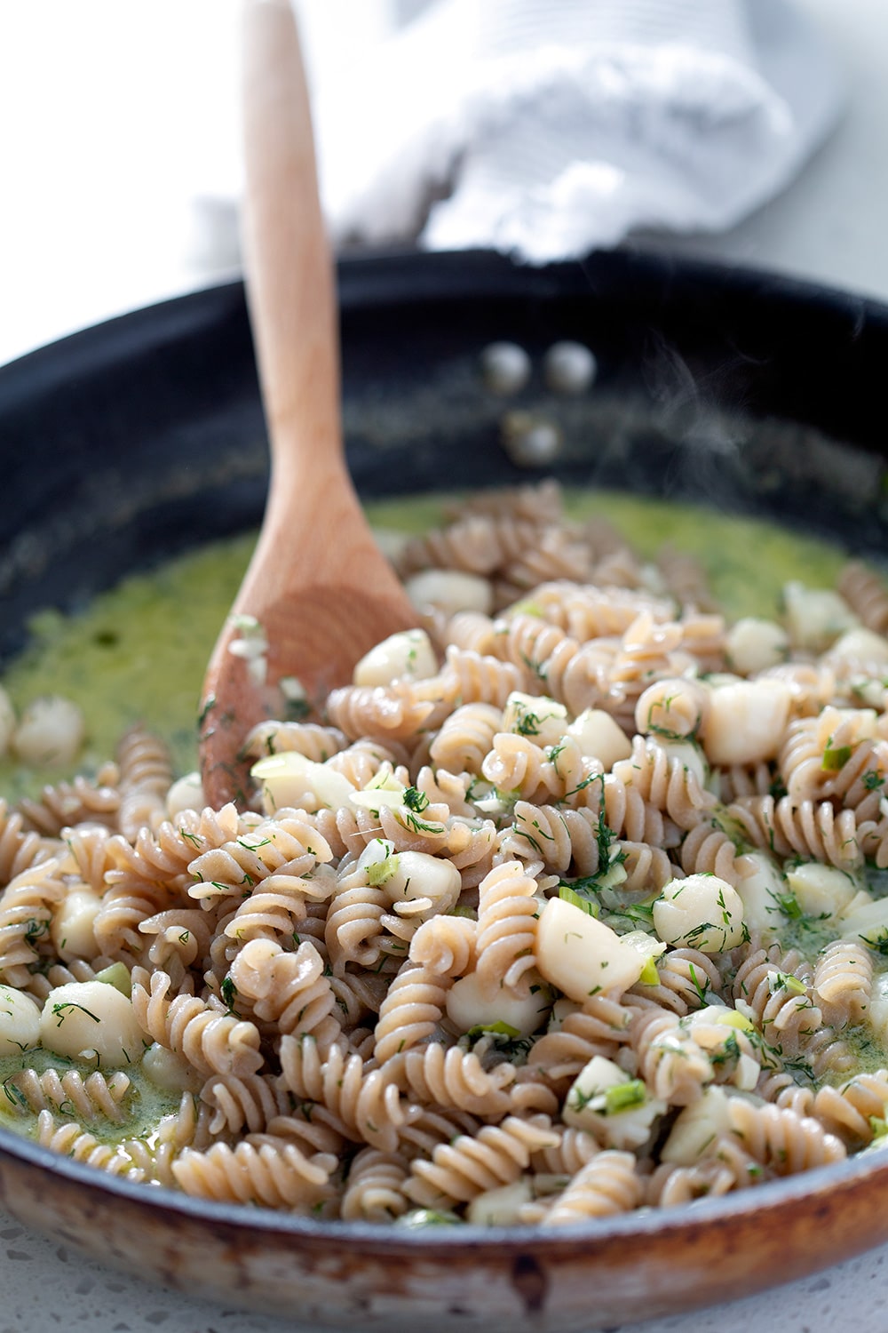 Dill scallop AIP pasta in the skillet with wooden spoon