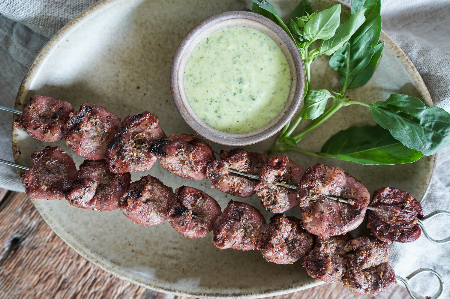  grilled chicken hearts on skewer with a green sauce on side